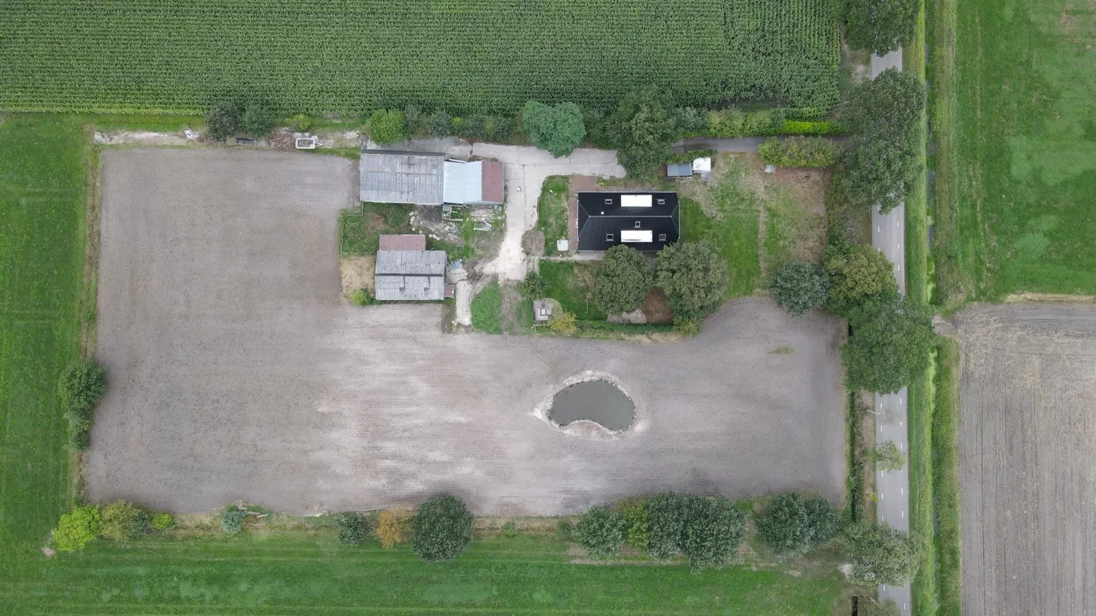 Dronefoto van hetzelfde perceel: het hele land is kale, bewerkte grond met in het midden een vijver