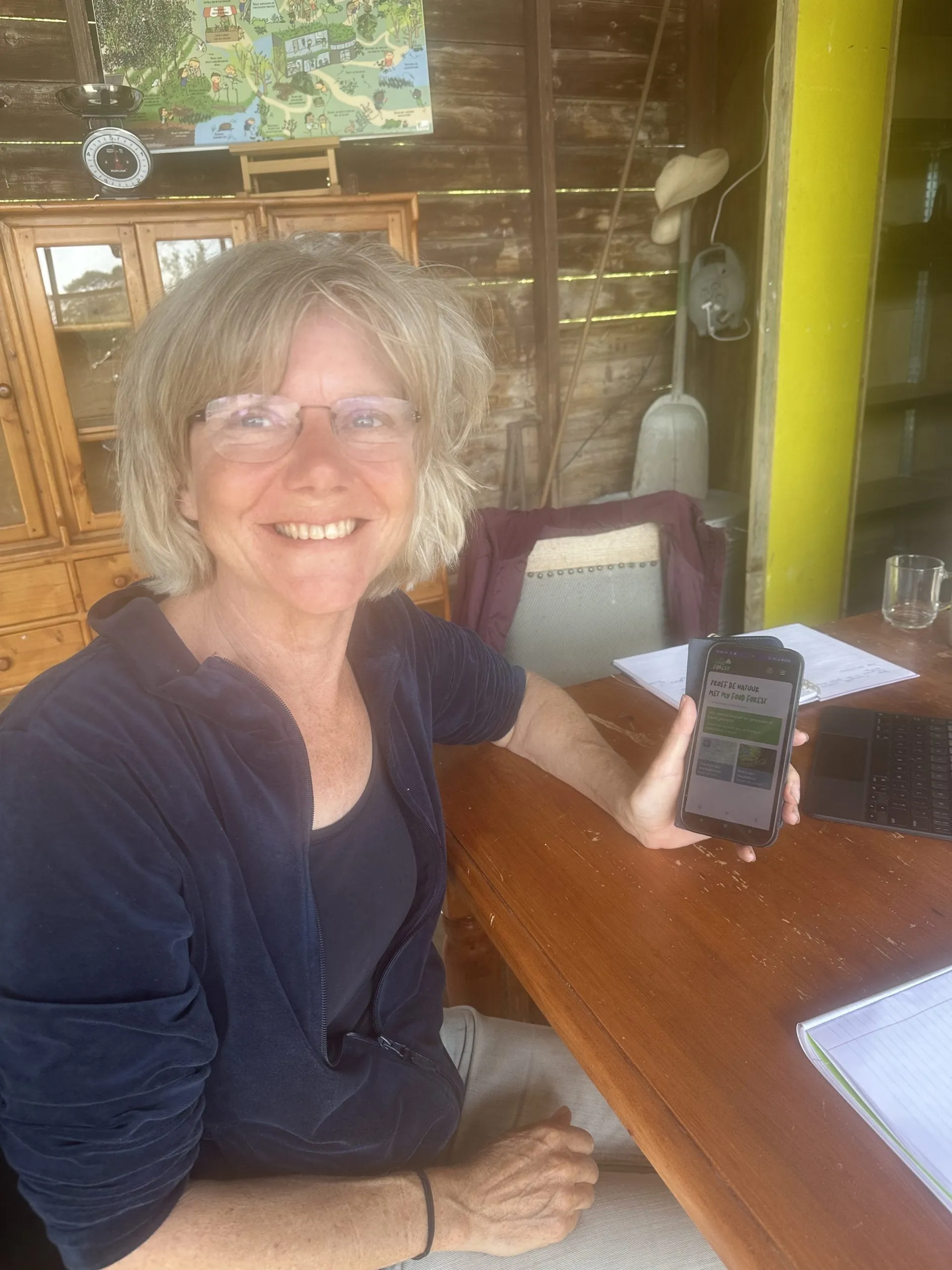 Lachende vrouw aan een houten tafel met een telefoon in haar hand