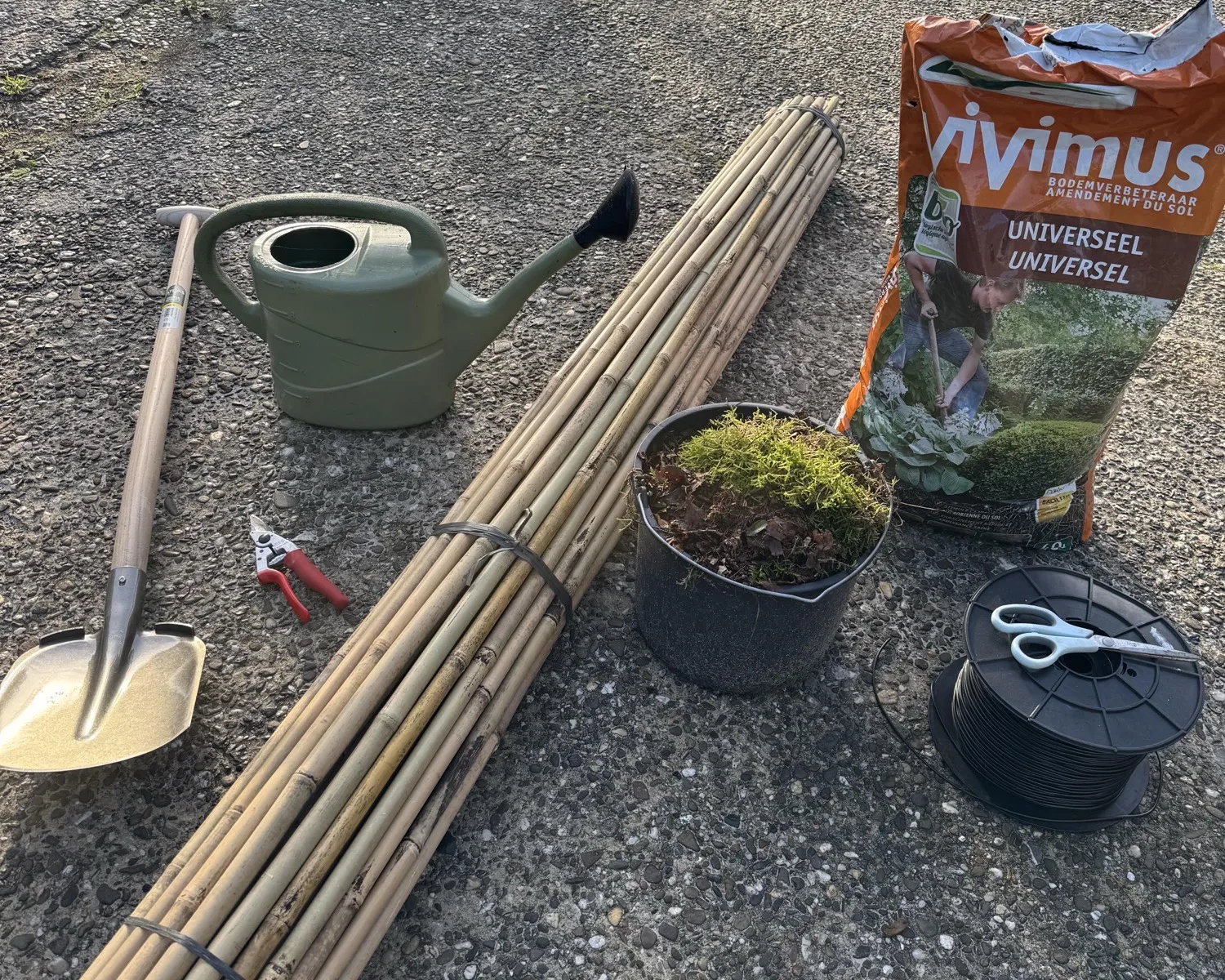 Spade, watering can, secateurs, bamboo canes, bucket of forest soil, bag of Vivimus and a spool of tree tie tubing with scissors on the ground