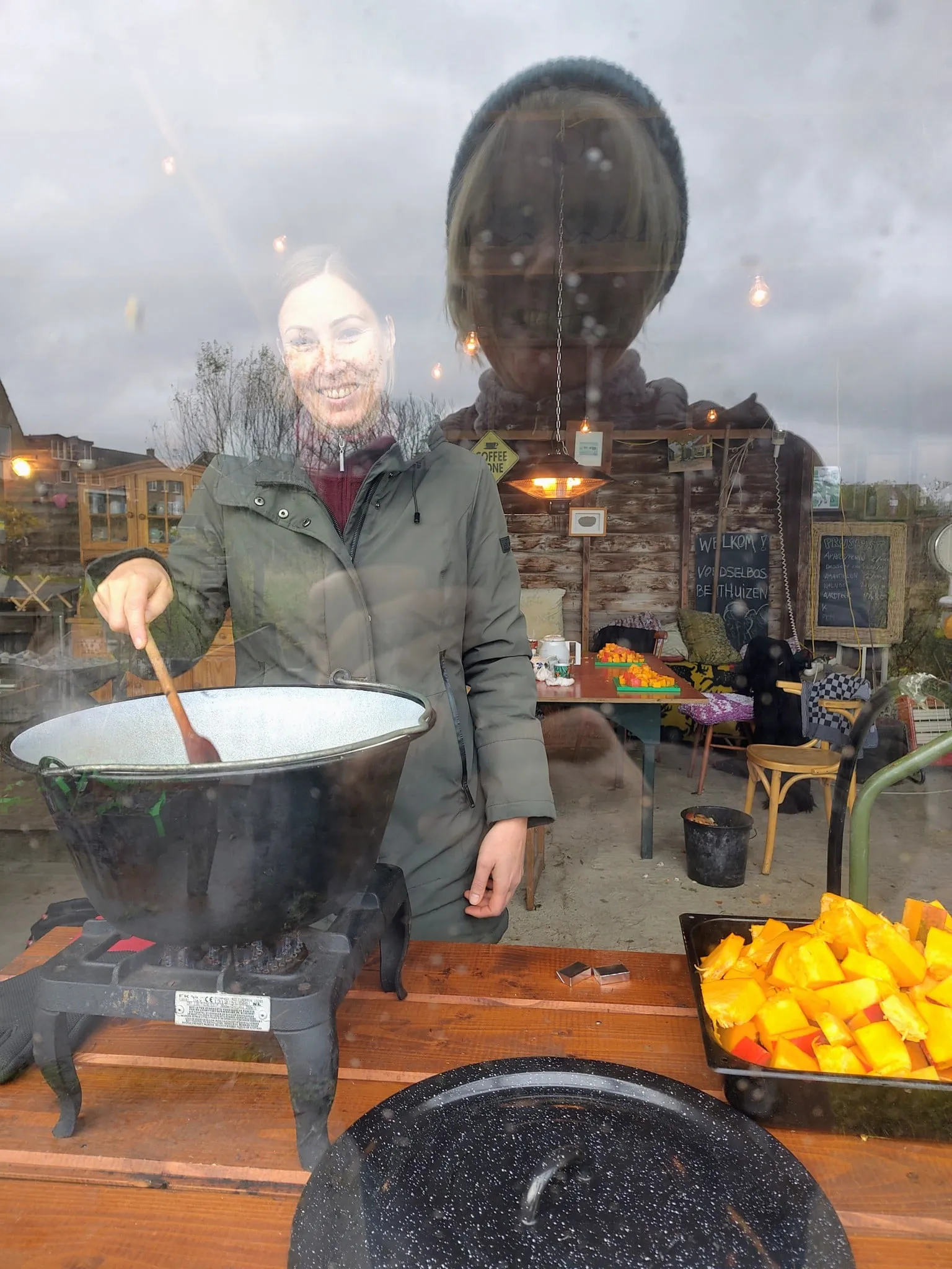 Vrouw roert in een grote pan soep, met blokjes pompoen ernaast