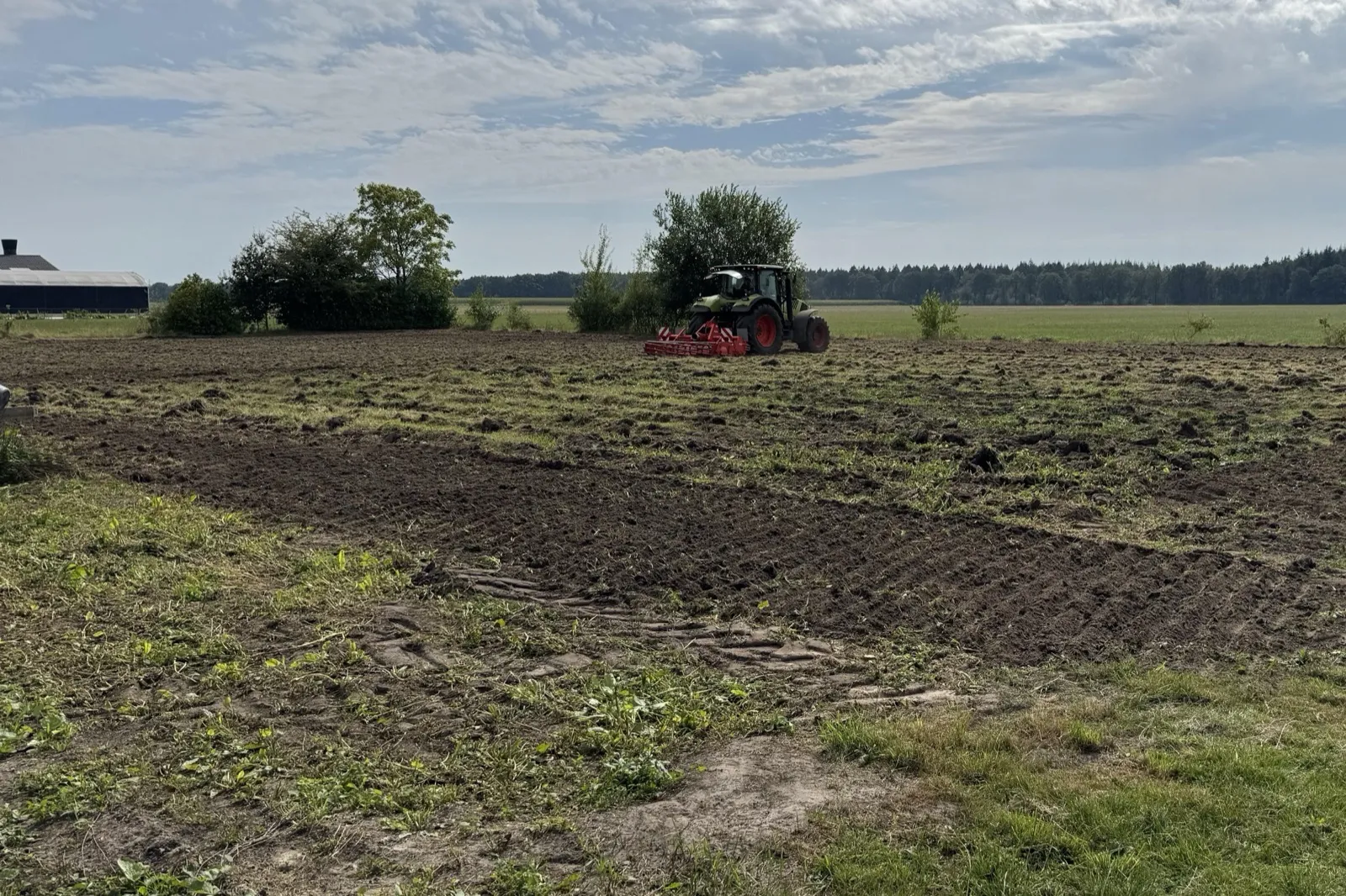 Een trekker met een rode frees achterop, op een strook pas gefreesde grond