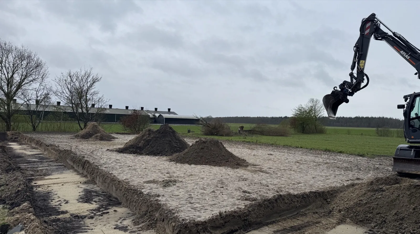 Een graafmachine bij de zandvlakte van de paardenbak, met hopen aarde op het zand
